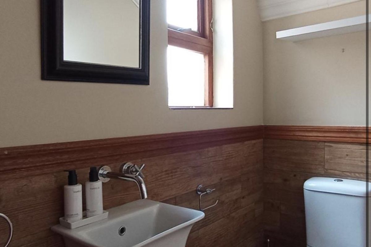 A compact bathroom featuring timber-look wall panelling, a wall-mounted basin with chrome fixtures, and a modern dual-flush toilet.