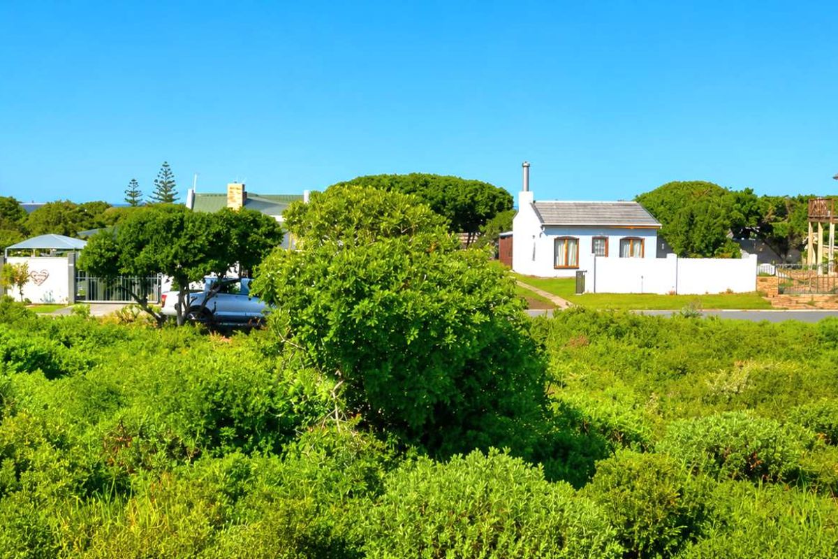 A view of a vacant residential plot covered in natural vegetation, surrounded by existing residential properties and boundary walls.