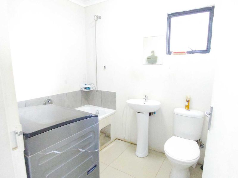 A functional bathroom featuring a pedestal basin, toilet, and shower area with tiled flooring and splashbacks.
