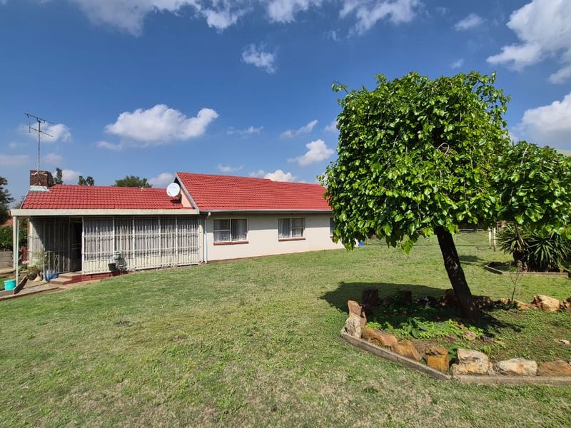 Rear view of the house featuring a tiled roof, an enclosed patio area, and a spacious garden with a mature tree.