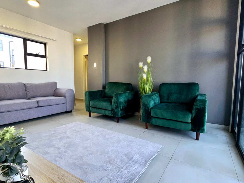 A bright living room featuring neutral tiled flooring, a dark accent wall, and a large sliding glass door providing natural light.