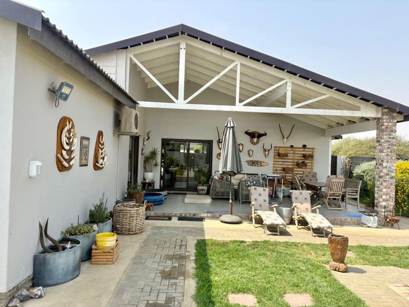 Spacious covered patio featuring exposed white roof trusses, tiled flooring, and direct access to the interior through large sliding glass doors.