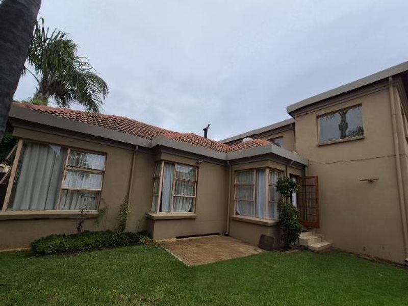 Rear view of the house featuring a tiled roof, bay windows, a small paved patio area, and a grass lawn.