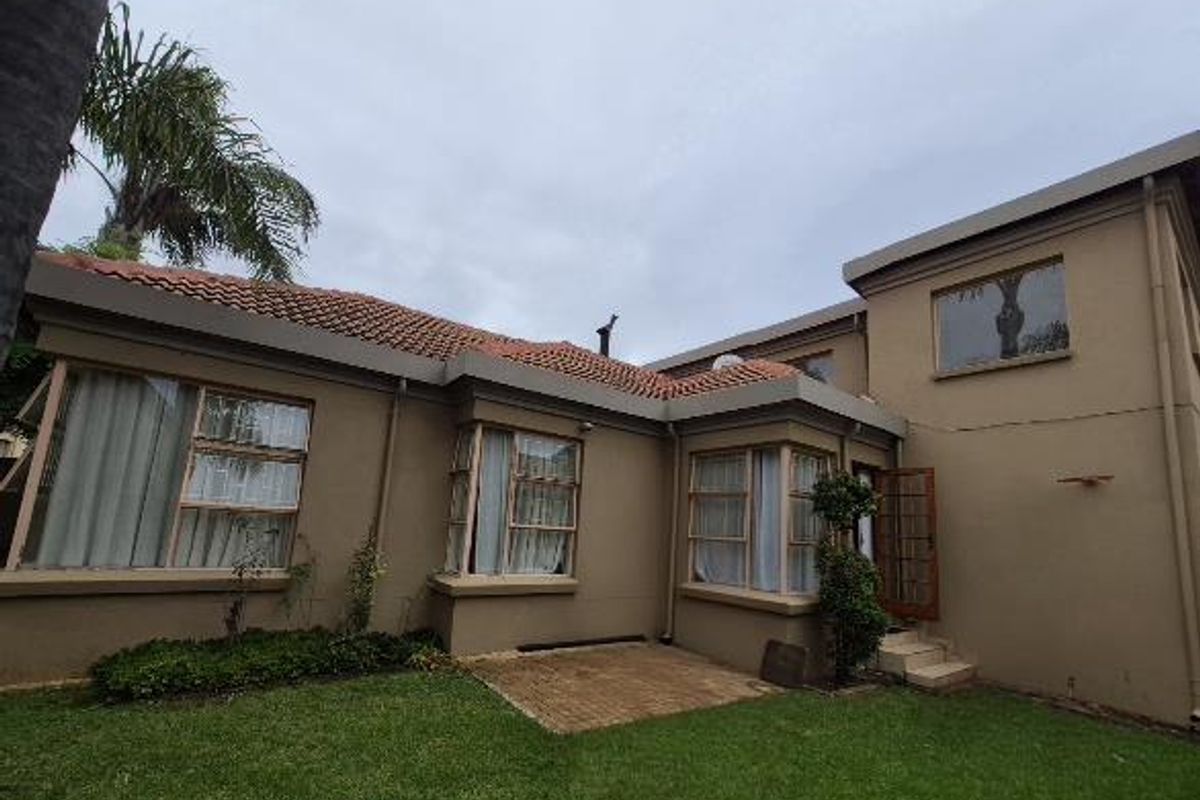 Rear view of the house featuring a tiled roof, bay windows, a small paved patio area, and a grass lawn.