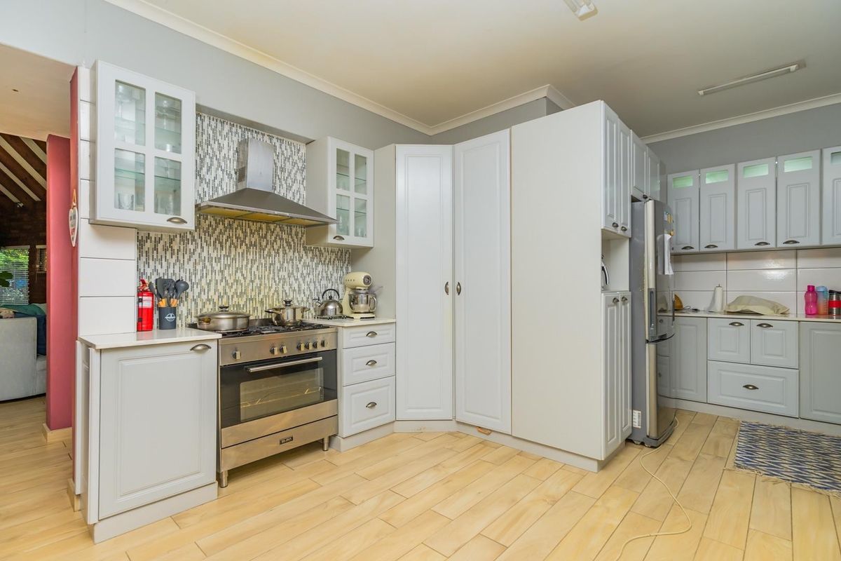 A well-maintained kitchen featuring light-toned cabinetry, a gas stove with stainless steel extractor fan, mosaic tile splashback, and durable laminate flooring.