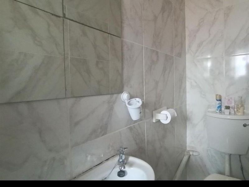 A compact bathroom featuring marble-effect wall tiling, a pedestal basin with chrome faucet, and a standard toilet with visible plumbing.
