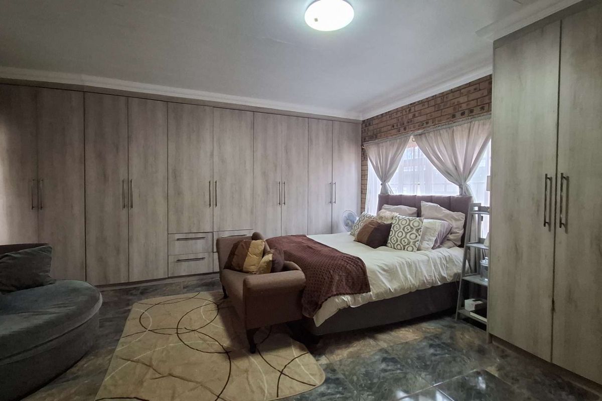 Spacious bedroom featuring extensive built-in cupboards, exposed brick accents, and durable tiled flooring, offering ample storage and a warm, textured aesthetic.
