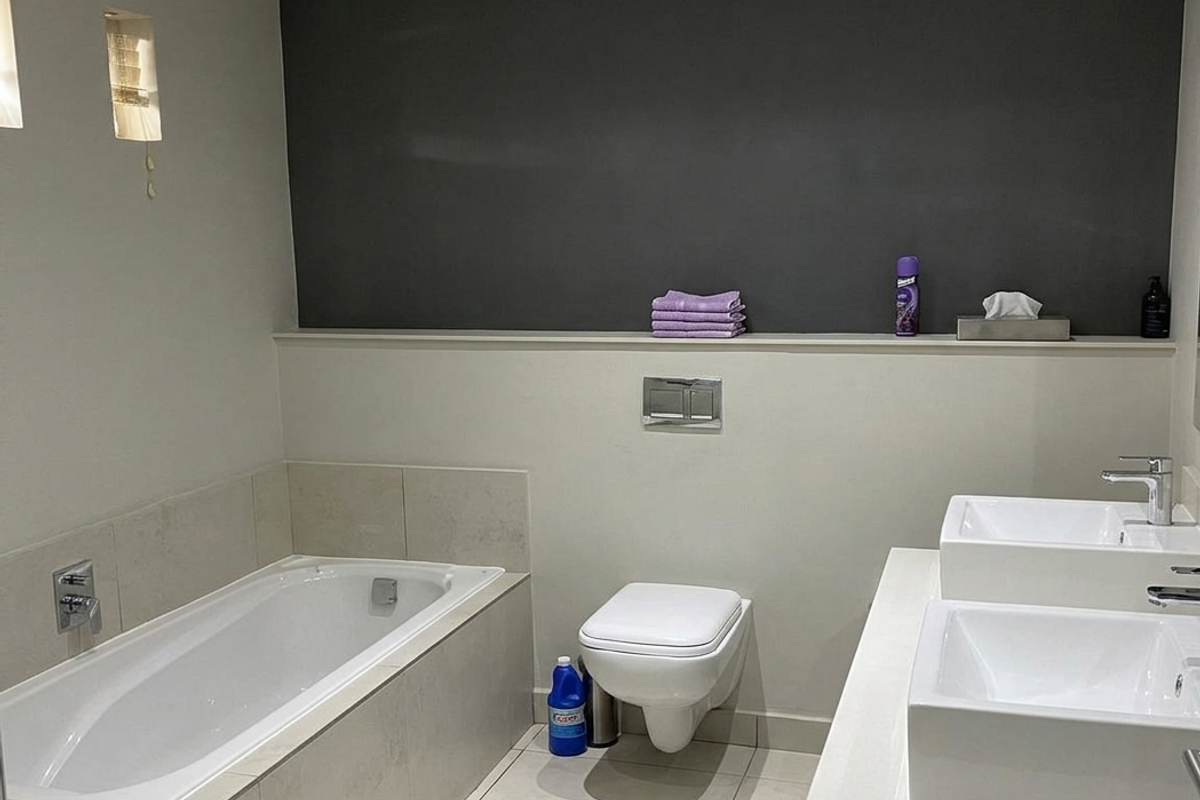 Modern bathroom featuring a built-in bathtub, wall-hung toilet, and a dual vanity unit with contemporary basin fixtures and neutral tiling.