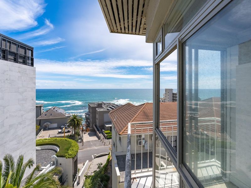 A scenic elevated view overlooking the coastal neighborhood and ocean, captured from a balcony with sliding glass doors.