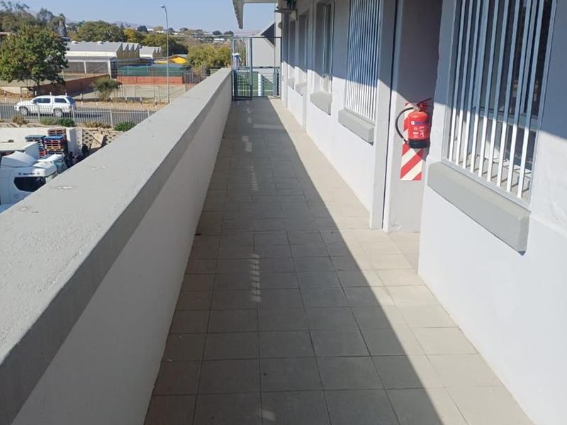 An exterior walkway or balcony featuring tiled flooring, security bars on windows, and mounted fire safety equipment.