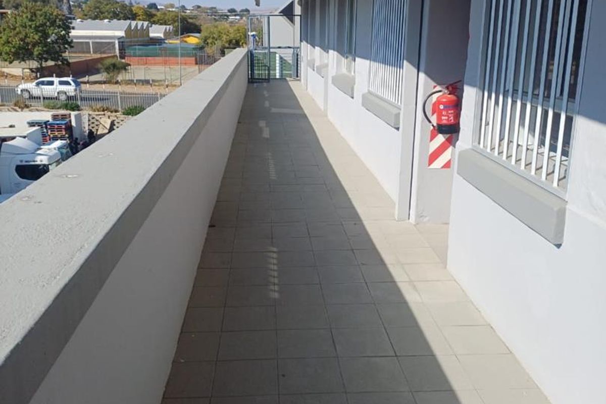 An exterior walkway or balcony featuring tiled flooring, security bars on windows, and mounted fire safety equipment.