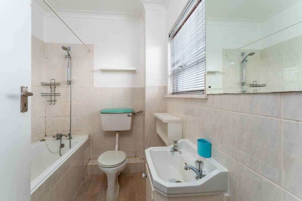 A dated bathroom featuring a standard bathtub with shower attachment, a pedestal sink, and a toilet, finished with neutral wall tiling.