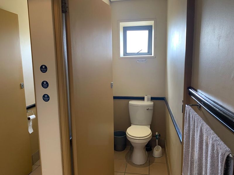 A functional office restroom featuring a standard toilet, tiled flooring, and a small window for ventilation.