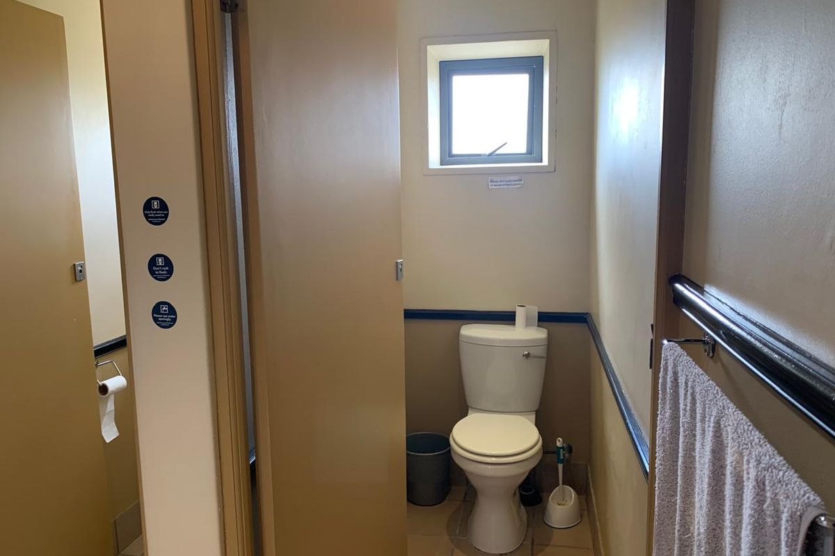 A functional office restroom featuring a standard toilet, tiled flooring, and a small window for ventilation.