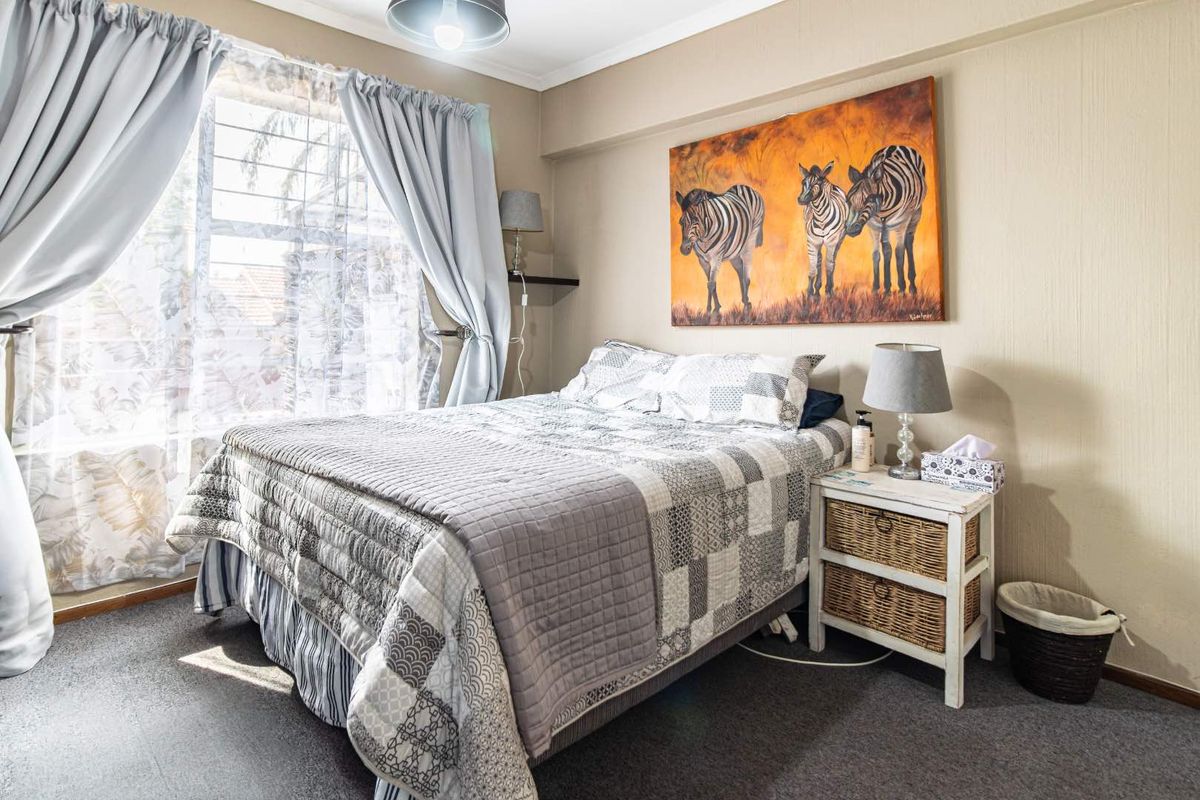 A cozy bedroom featuring carpeted flooring, a louvered window with natural light, and classic ceiling cornicing.