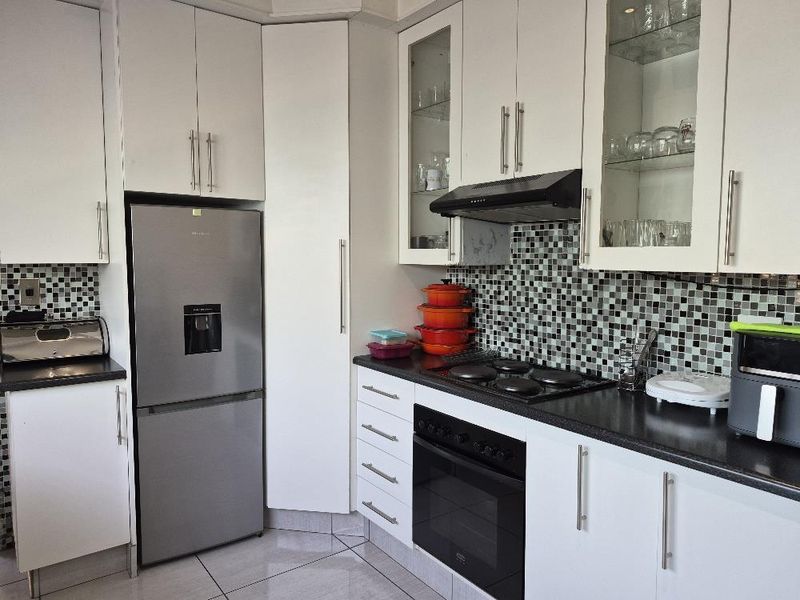A functional kitchen featuring white cabinetry, mosaic tile backsplash, dark countertops, and integrated appliances including an oven and hob.