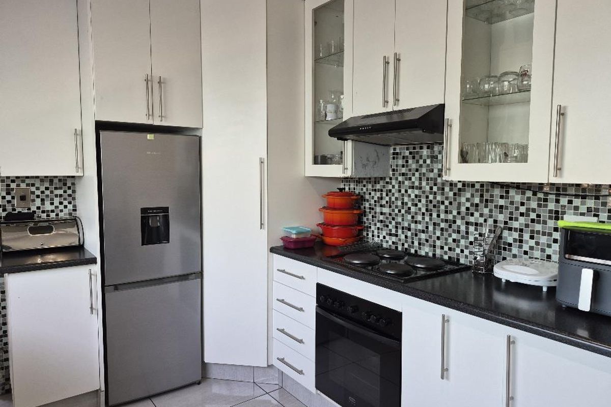 A functional kitchen featuring white cabinetry, mosaic tile backsplash, dark countertops, and integrated appliances including an oven and hob.