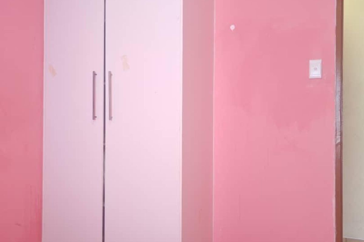 A bedroom featuring a built-in white wardrobe, tiled flooring, and pink painted walls.