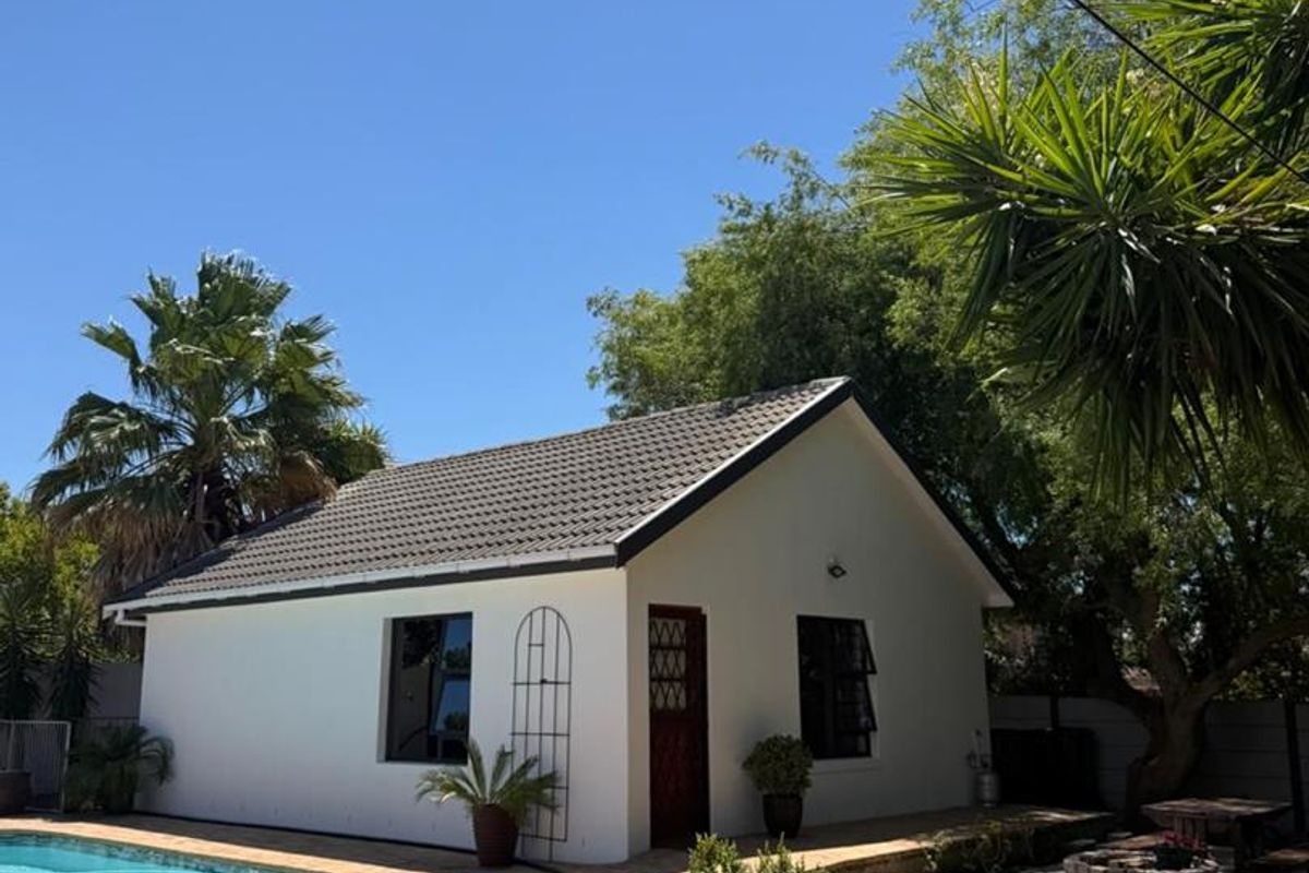 A well-maintained cottage exterior featuring a tiled roof, paved patio area, and direct access to a swimming pool in a landscaped garden setting.