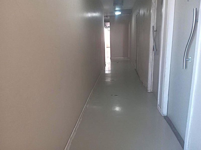 A narrow apartment hallway featuring flush-mounted doors and recessed ceiling lighting, showing signs of wear on the flooring and walls.