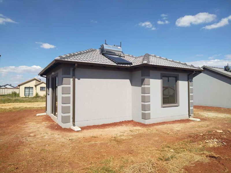 Rear view of a modern single-story house featuring a tiled roof, solar water heating system, and exterior wall detailing.