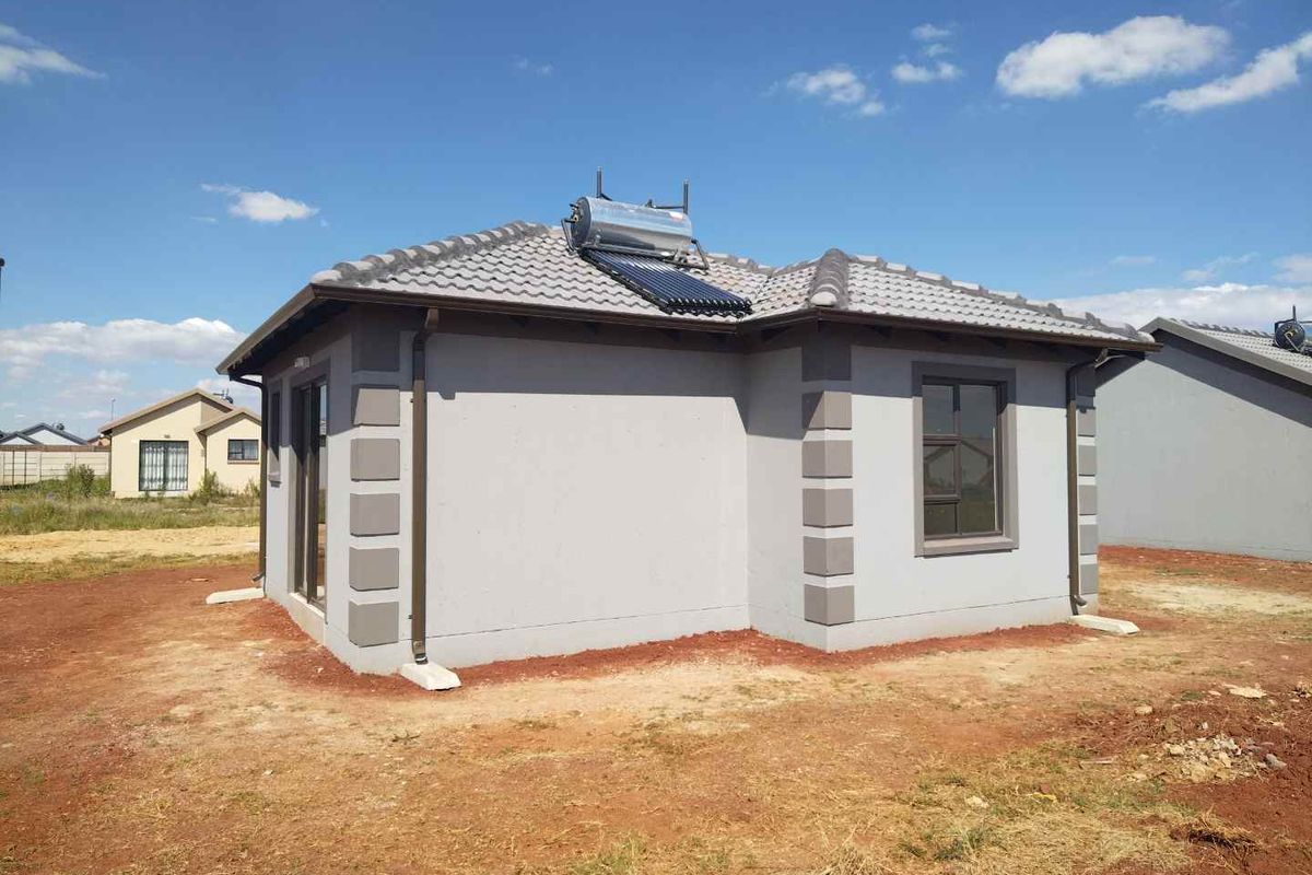 Rear view of a modern single-story house featuring a tiled roof, solar water heating system, and exterior wall detailing.