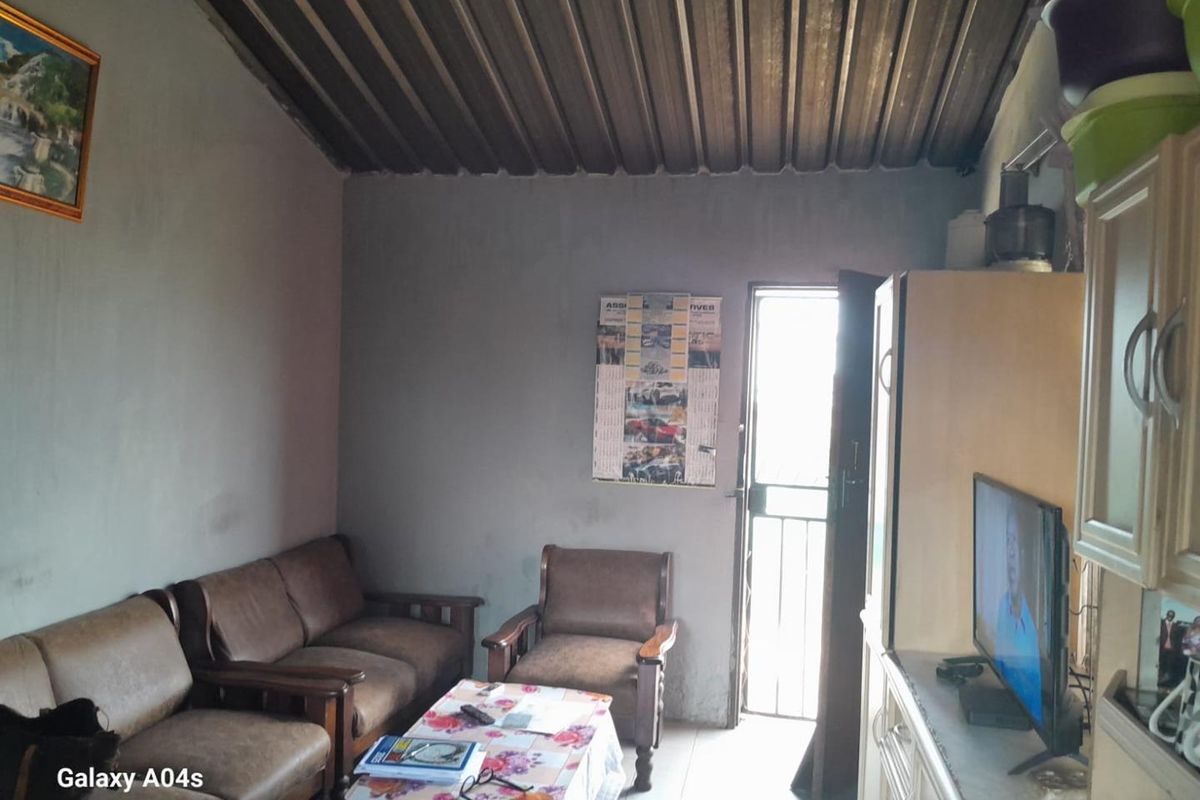 A modest living room featuring exposed corrugated metal roofing and a security gate entrance.