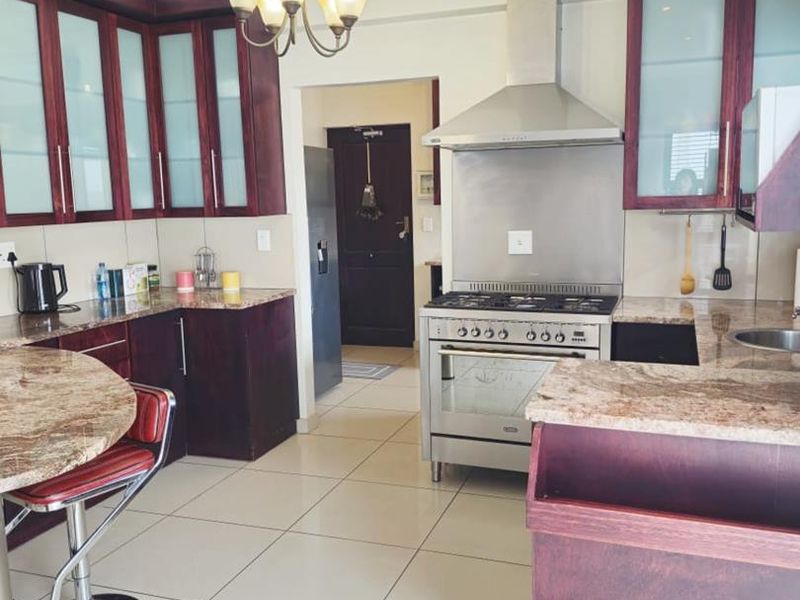 A functional kitchen featuring dark wood cabinetry, granite countertops, stainless steel gas stove with extractor, and tiled flooring.