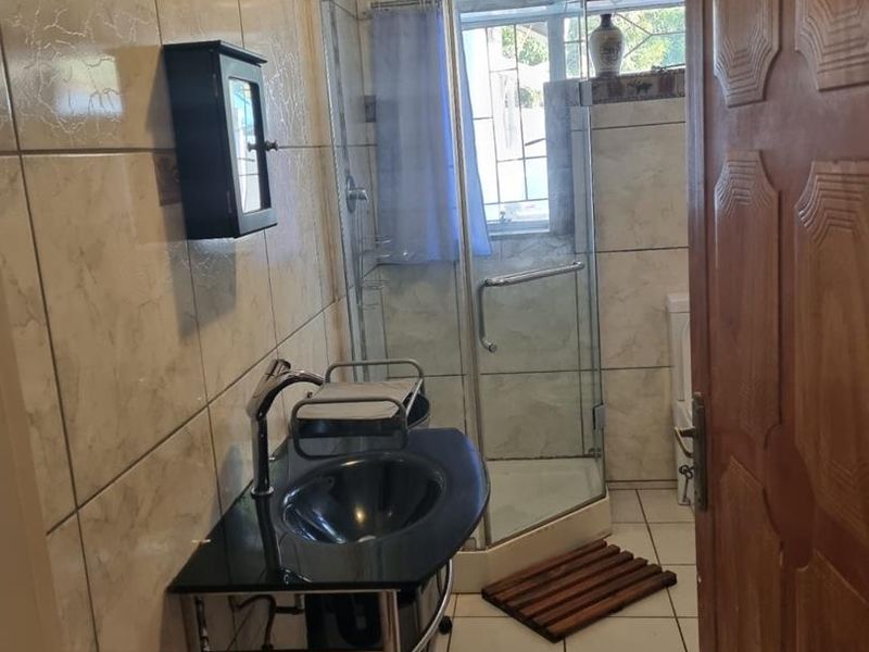 A functional bathroom featuring tiled walls and flooring, a corner shower enclosure, and a modern wall-mounted basin with a sleek mixer tap.