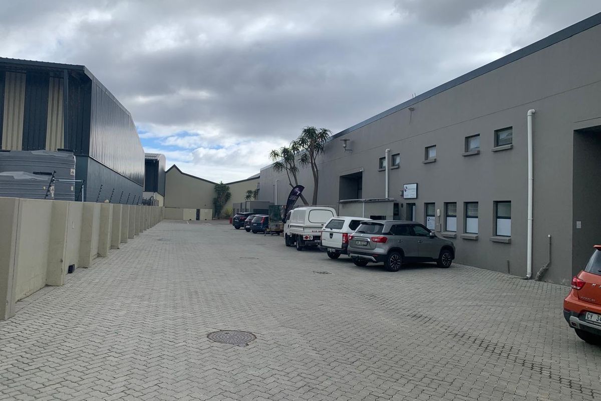 Exterior view of an industrial property featuring a paved parking area, concrete boundary walls, and modern warehouse building facades.