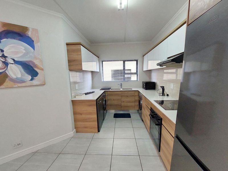 Modern galley-style kitchen featuring wood-finish cabinetry, white stone countertops, integrated appliances, and tiled flooring with ample natural light.