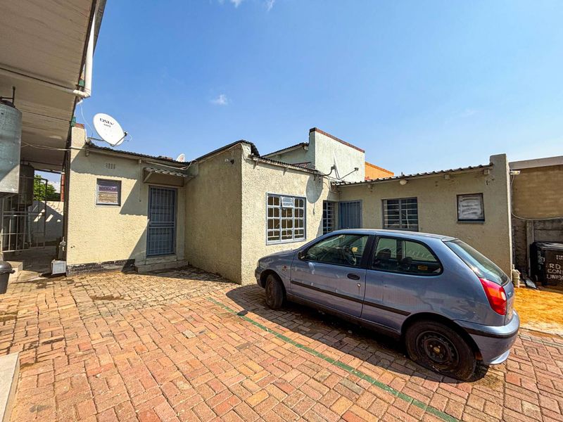 Rear exterior view of the property featuring a brick paved courtyard, plastered walls, and steel window frames with security gates.