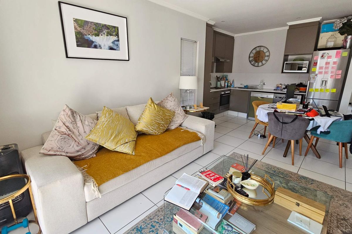 Open-plan living area featuring a modern kitchen with built-in cabinetry, oven, and hob, seamlessly flowing into a comfortable lounge space with tiled flooring throughout.