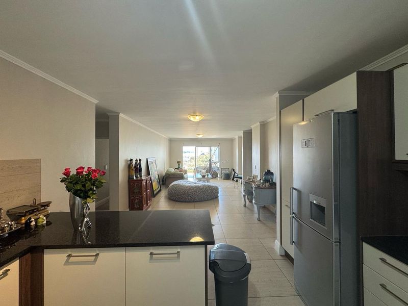 Open-plan living area featuring a modern kitchen with granite countertops and tiled flooring, flowing into a spacious lounge with access to a balcony.