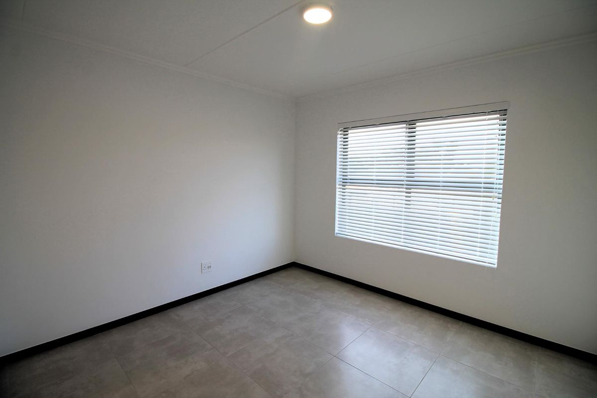 A clean, empty bedroom featuring neutral tiled flooring, white walls, and a window fitted with venetian blinds.