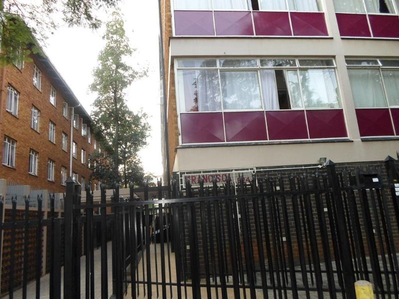 Exterior view of a multi-story apartment building featuring brick facade, metal security fencing, and large windows.
