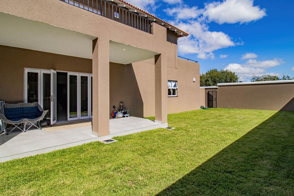 A spacious rear exterior featuring a covered patio with tiled flooring, a well-maintained lawn, and a balcony above with a metal balustrade.