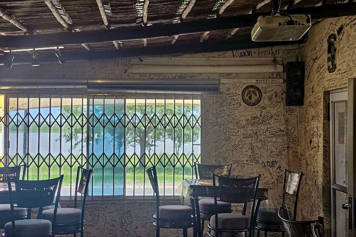 A rustic indoor entertainment area featuring a thatched roof, projector, and walls covered in writing, with security gates over the windows.