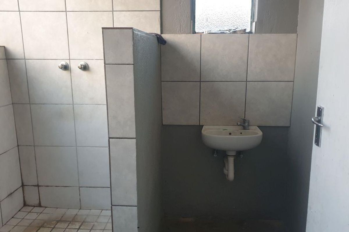 A functional bathroom space featuring a tiled shower area and a wall-mounted basin, requiring cosmetic updates and maintenance.