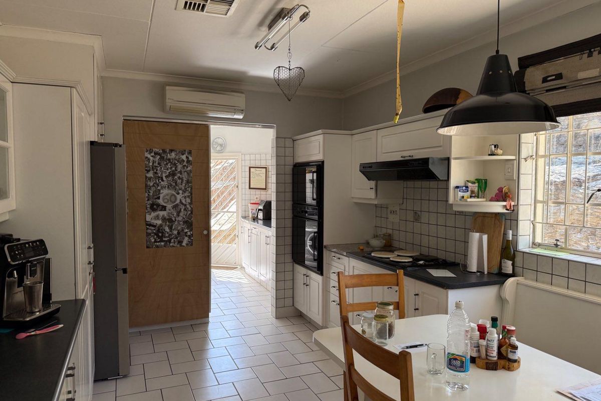 A functional kitchen featuring built-in cabinetry, integrated oven, hob, extractor fan, and tiled flooring, with an adjacent scullery area.
