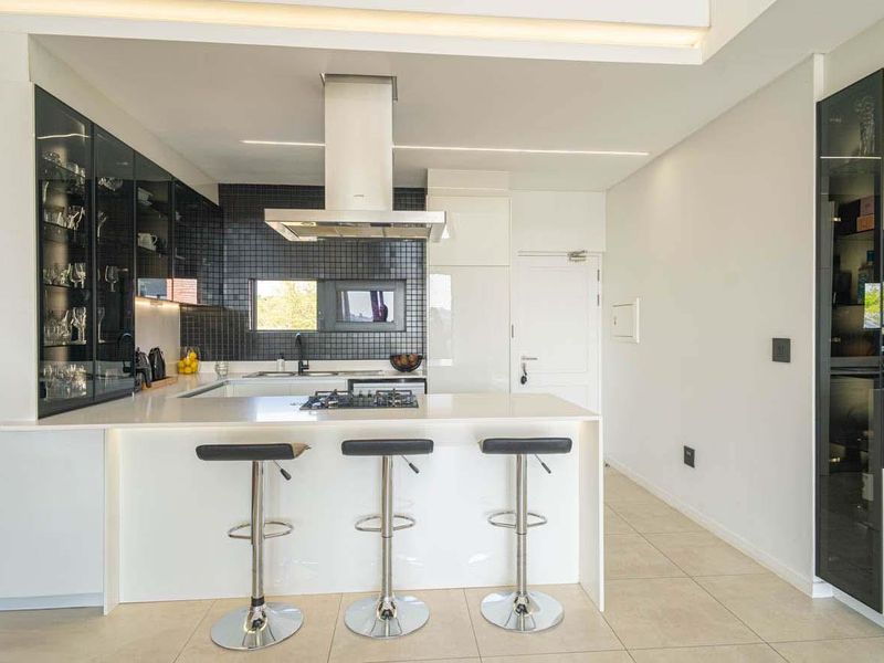 Modern kitchen featuring a central island with gas hob, integrated appliances, sleek cabinetry, and a stylish exposed brick feature wall.