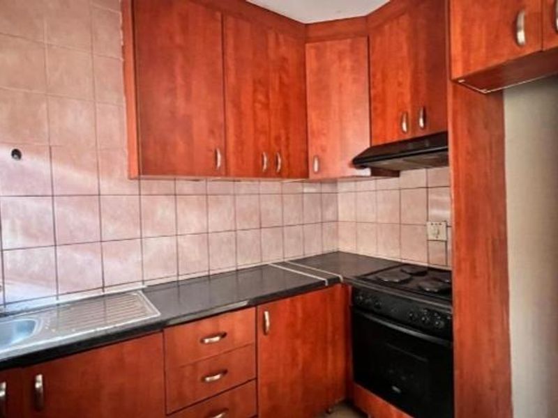A functional kitchen featuring wood-tone cabinetry, dark countertops, a built-in oven with hob, and a stainless steel sink with tiled splashback.
