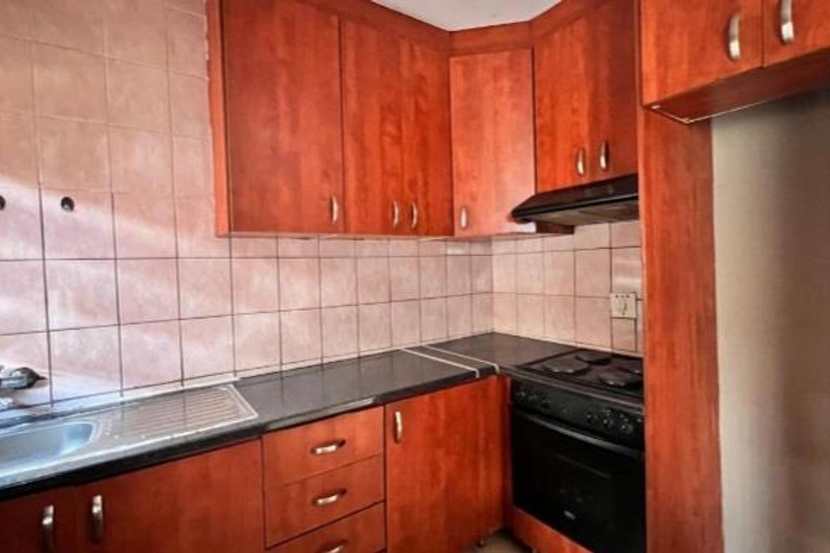 A functional kitchen featuring wood-tone cabinetry, dark countertops, a built-in oven with hob, and a stainless steel sink with tiled splashback.