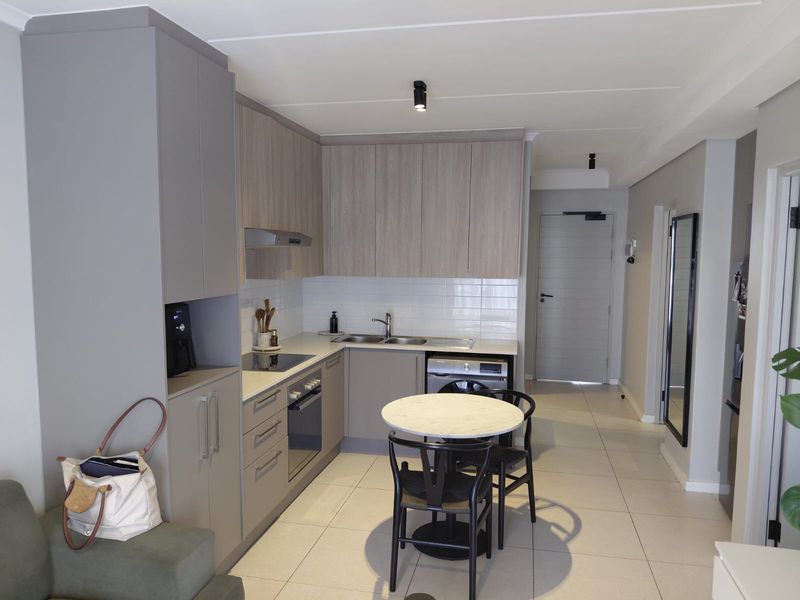Modern open-plan kitchen featuring sleek cabinetry, integrated appliances, tiled flooring, and efficient recessed lighting, seamlessly connecting to the living area.