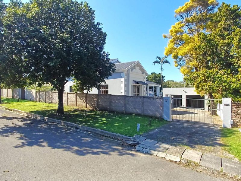 Front view of the property featuring a paved driveway, metal gate, brick boundary wall, and a detached garage structure.