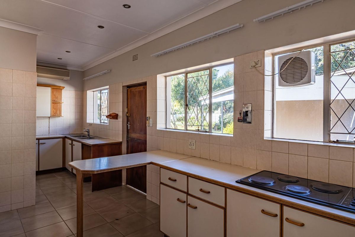 A functional kitchen featuring built-in cabinetry, a fitted electric hob, tiled splashbacks, and large windows providing natural light and garden views.