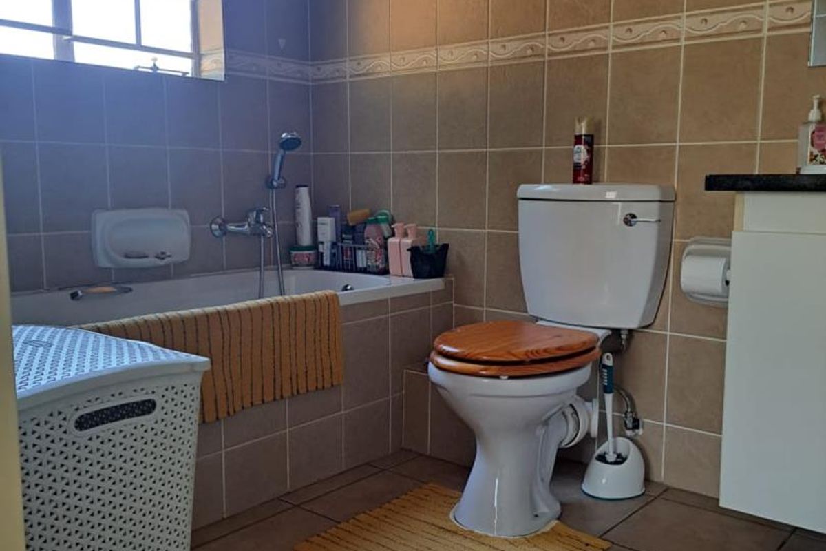 A functional bathroom featuring a built-in bathtub with shower mixer, a standard toilet, and tiled wall and floor finishes.