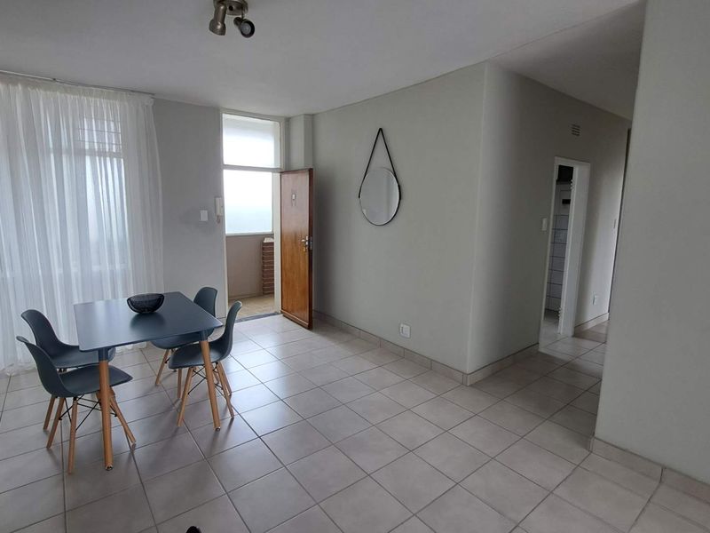 Open plan living and dining area featuring neutral tiled flooring, access to a balcony, and a functional layout connecting to the hallway.