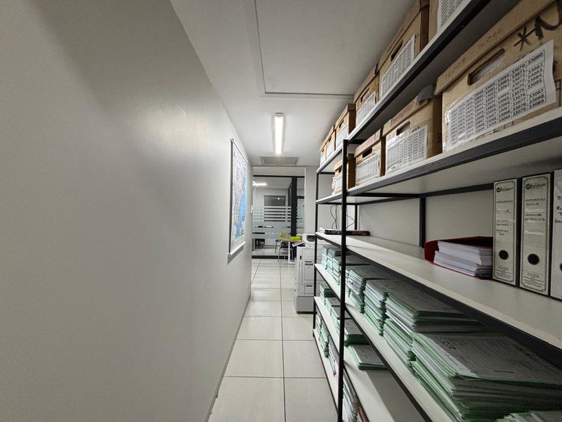 A functional office hallway featuring tiled flooring and overhead fluorescent lighting, providing access to adjacent workspace areas.