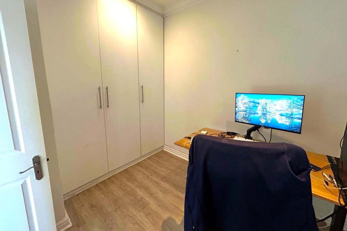 A functional bedroom featuring built-in floor-to-ceiling wardrobes and durable wood-look laminate flooring.